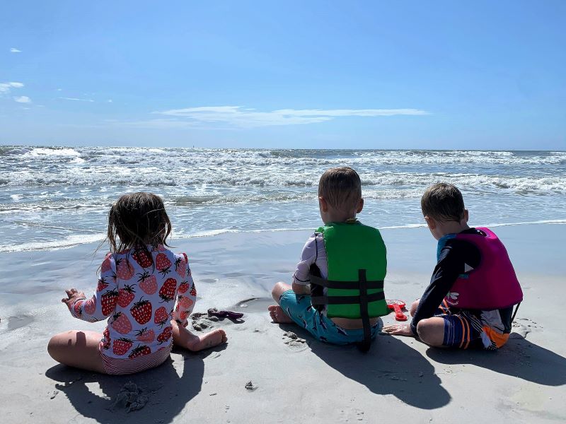 Young children in life jackets and swim clothes at the beach.