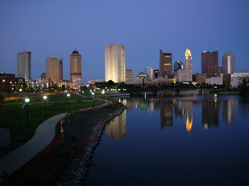 Columbus, Ohio skyline at night, showing skyscrapers lit up and reflected on the Scioto River.