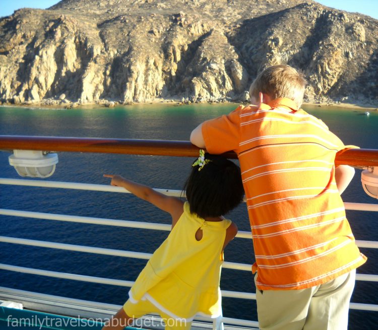 Two kids standing at deck rail of a cruise ship modeling their cruise wardrobe -- her in a comfortable, lightweight knit outfit, and him in a lightweight polo with khakis.
