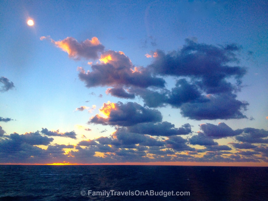 Sunset over the ocean with blue clouds, orange sun across the horizon and deep blue sea.