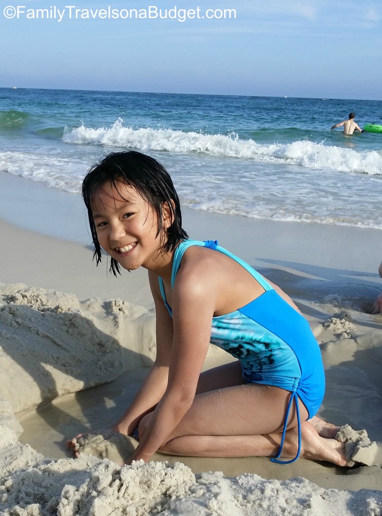 Girl in blue swimsuit with big smile, digging in the sand at the beach.