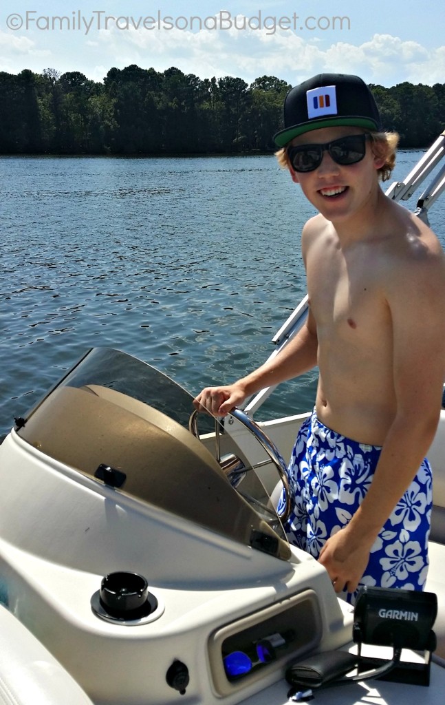 Young man in sunglasses and a blue swimsuit driving a boat.