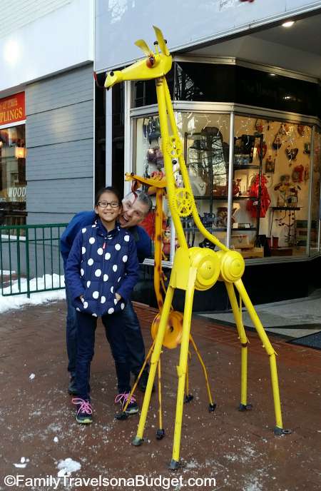 Dad and daughter standing next to metal art giraffes outside a local shop in  downtown Charlottesville VA.