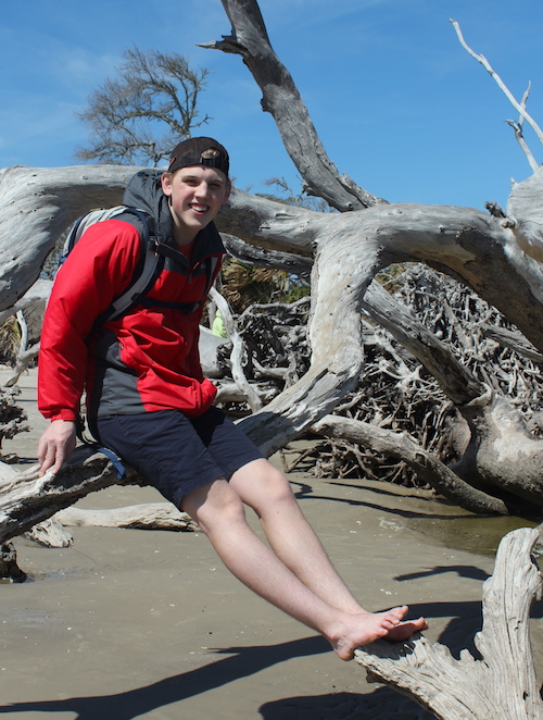 Teenager sitting on petrified wood at Driftwood Beach Jekyll Island. 