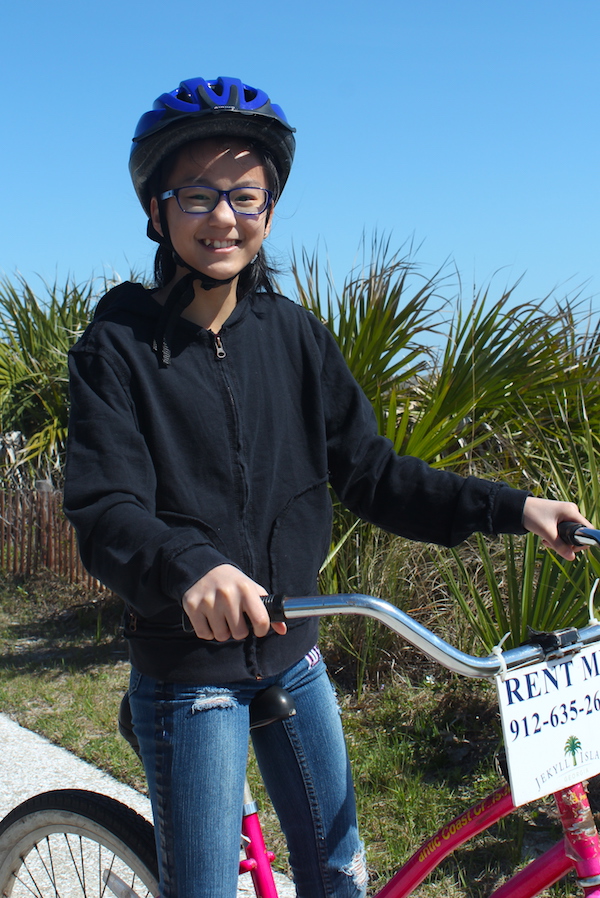 Girl on pink bike with black hoodie and helmet. 