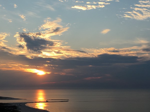 The sun glows orange over the Gulf of Mexico as clouds streak across the sky