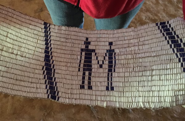 white wampum belt with blue beading showing two people shaking hands