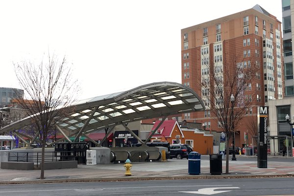 DC Metro Station for Clarendon Station showing the Metro Sign with colored route stripes and covered escalators down to the station.