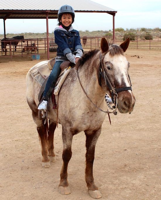 Young girl on horseback with a helmet and a really big smile.