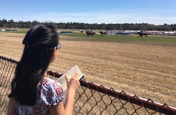 Standing trackside with her race day guide to watch the horses.