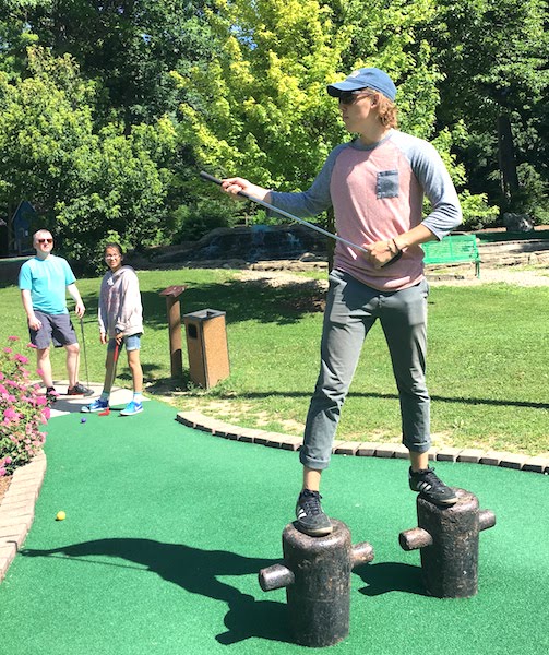 Our son being a goofball at the miniature golf course at Perry's Cave Family Fun Center while the family looks on.