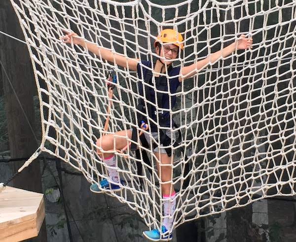 Teen girl in climbing net with safety gear at Xtreme Park Ropes Course in Durham.