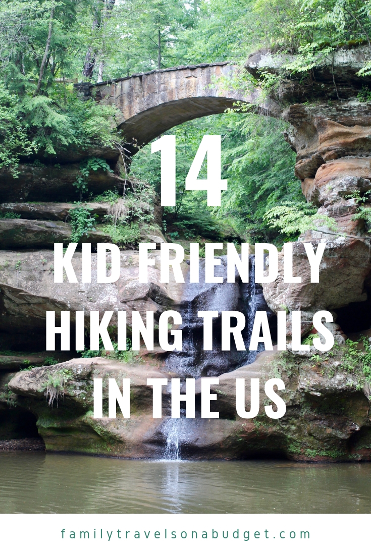 Stone bridge over a waterfall with forest all around, and title saying "14 of the best kid friendly hiking trails in the US." 