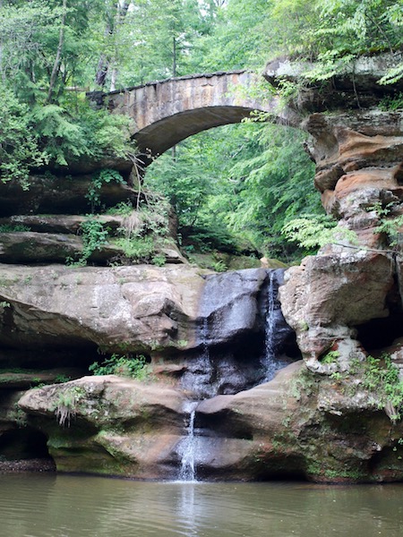 Hocking Hills waterfall with stone bridge above, one of the best family hiking vacation destinations in the US