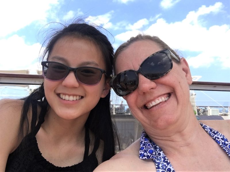 Mother and daughter in sunglasses on a pool deck on a cruise.