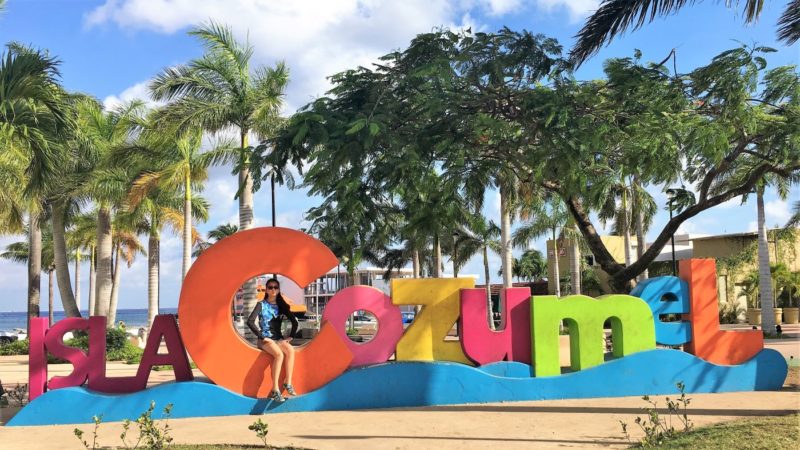 Ellie sitting on the Isla Cozumel sign downtown.