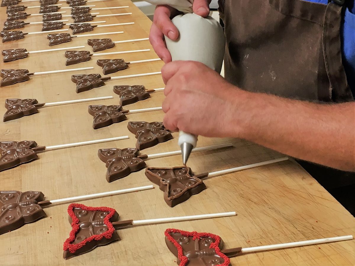 Hand made butterfly lollipops at Chocolates by Leopold with man piping chocolate details on the wings.