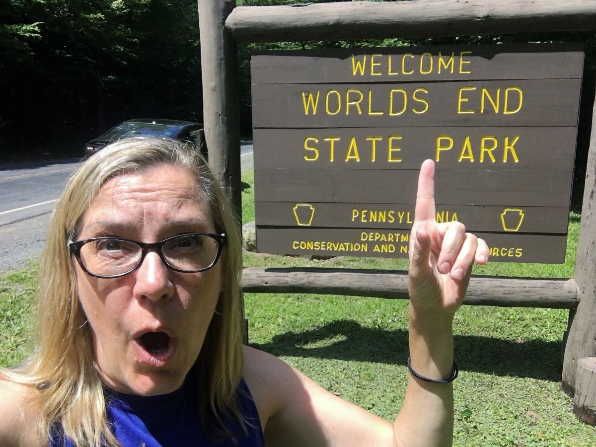 Pointing to the words "Worlds End" in the Endless Mountains state park sign with a surprised expression.