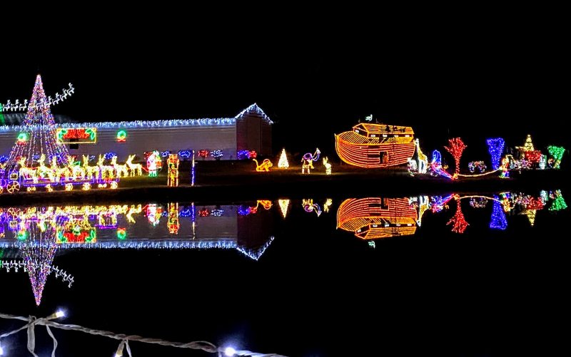 Christmas light display of Santa and Noah's ark reflected on the water.