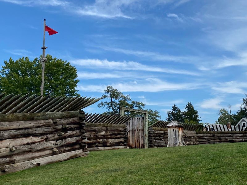 Perimeter wall at Fort Ligonier, built of timber with outward facing spiked logs, guard house and British flag