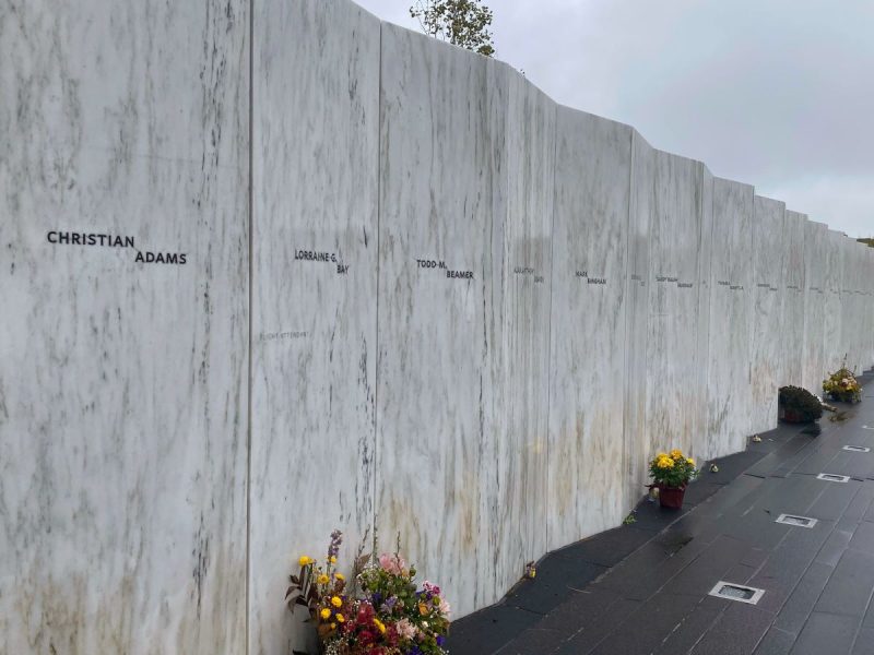 Wall of Names at the Memorial Walkway, a white marble wall that is uplit at night with flowers left at the base.