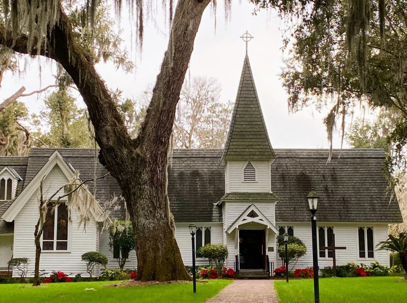 Christ Church Frederica on St Simons Island with brick walkway leading to entrance and stately oak tree draped in spanish moss