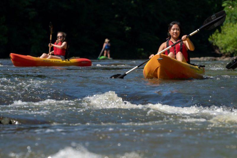 Women kayaking in yellow kayaks wearing red life jackets on the Rivanna River in Charlottesville