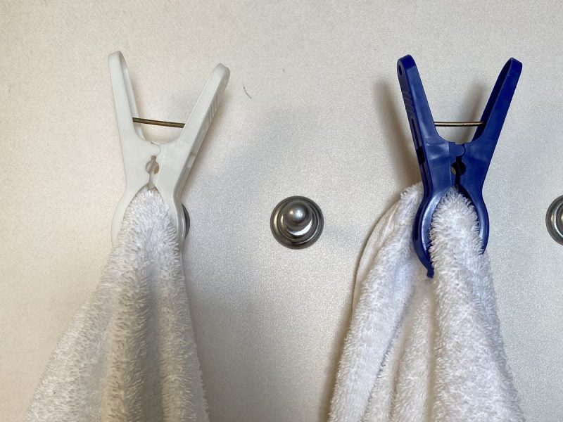 towels hanging on a bathroom door with blue and white clips, essential travel accessories for a cruise to keep the bathroom organized