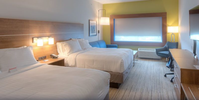 Holiday Inn Express hotel near Carowinds room with sleek, minimal design. Room here shows two bed configuration with a yellow accent wall, blue sofa and chair, and white bed covers