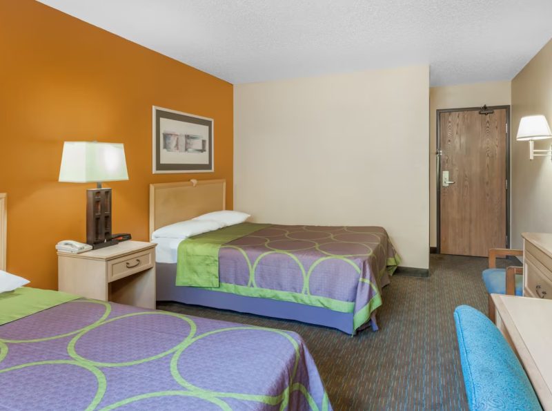 Super 8 by Wyndham is a hotel close to Carowinds good for the budget traveler who wants an inexpensive stay. Beds here shown with purple and green covers, with blue furniture and a pumpkin orange accent wall.