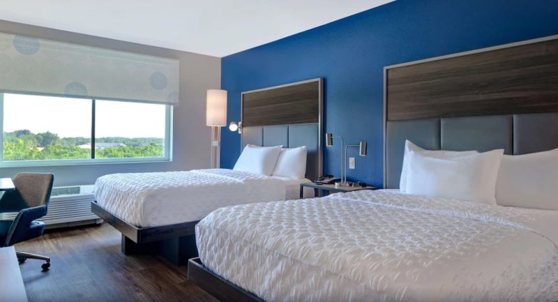 Double room at Tru by Hilton hotel near Carowinds with two queen beds covered in white duvets, with a navy blue accent wall behind and modern light fixtures.