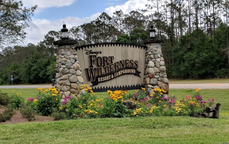Entrance sign for Fort Wilderness Rest & Campground in Florida with wildflowers in yellow and pink.