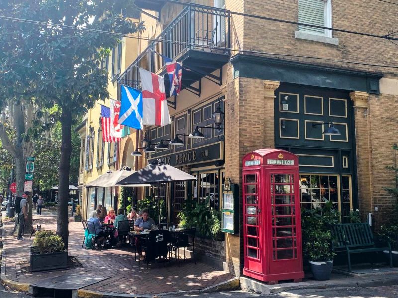 Exterior of Six Pence Pub in Savannah, yellow brick building with international flags and red phone booths