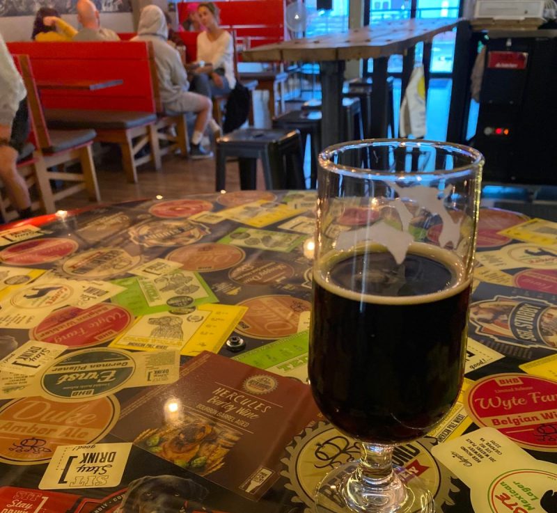 Beer Hound Brewery, Culpeper, VA restaurants. Shows a dark beer on a table made of beer labels with diners in the background.