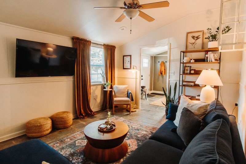 Living room of rental house with front entry beyond. Shows couch, TV, ceiling fan and open windows in a bright, airy space in Culpeper, VA