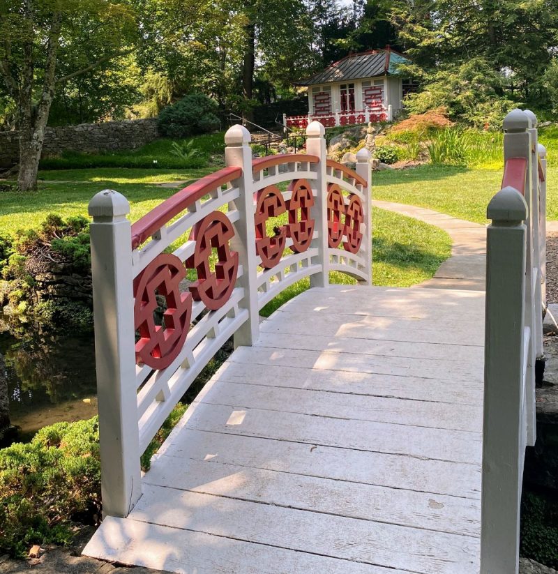 White bridge with red, Asian style medallions and a white and red tea house in the gardens at Glen Burnie House