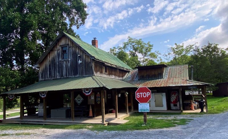 Cove Campground Office and camp store in Gore, VA. Rustic cabin with green metal roof, stop sign, grill and bunting. Blue sky and clouds behind