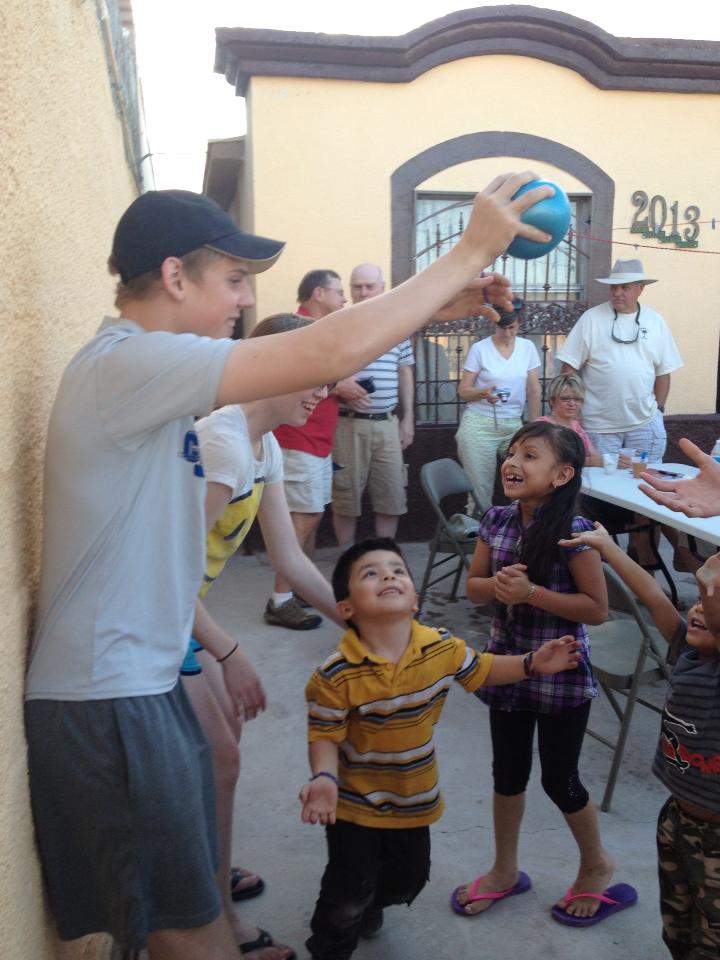 Teen boy in blue baseball hat plays with little kids on a Mexico missions trip.