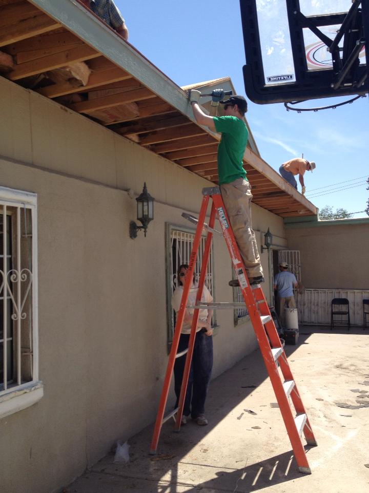 Teen on an orange ladder removing soffit to prepare a building for a new roof.