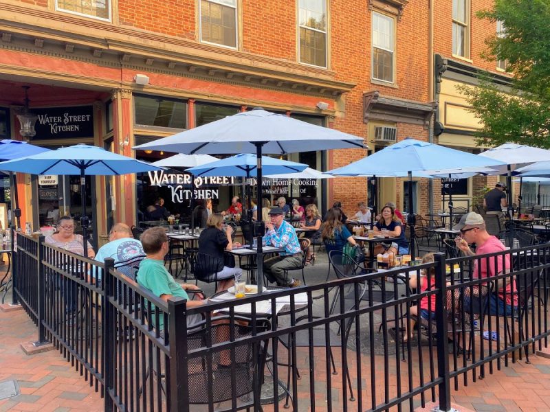 People sitting at outdoor tables under blue umbrellas at a restaurant in Old Town Winchester, Virginia
