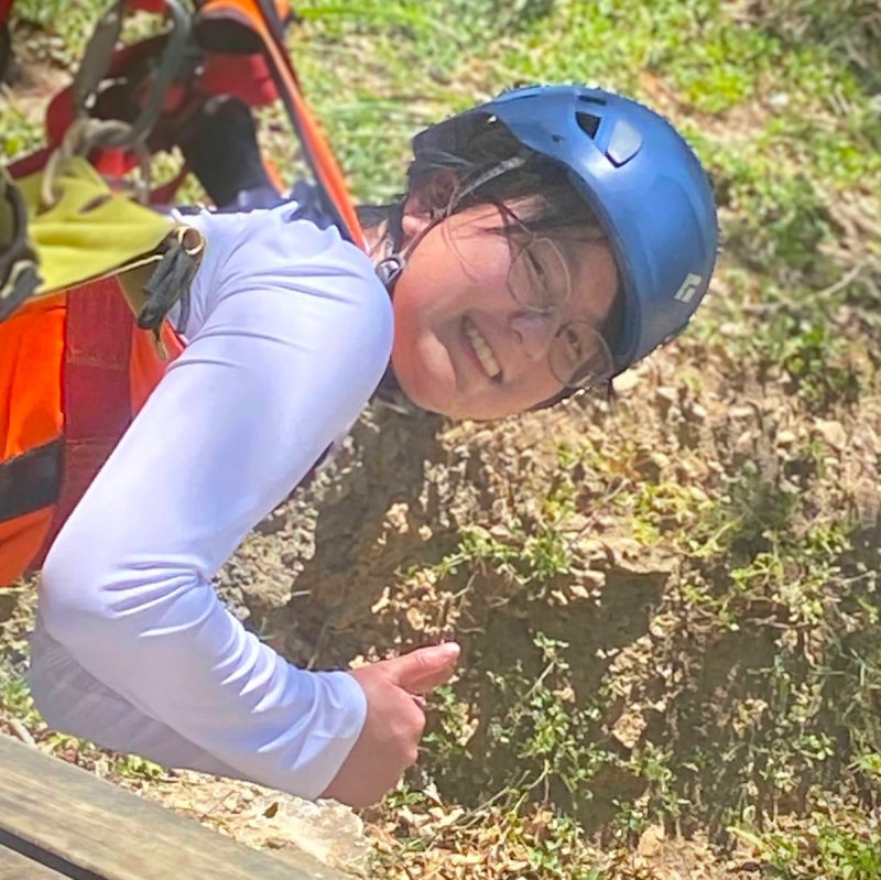 Young woman in helmet and zip line harness wearing a long sleeve sun shirt