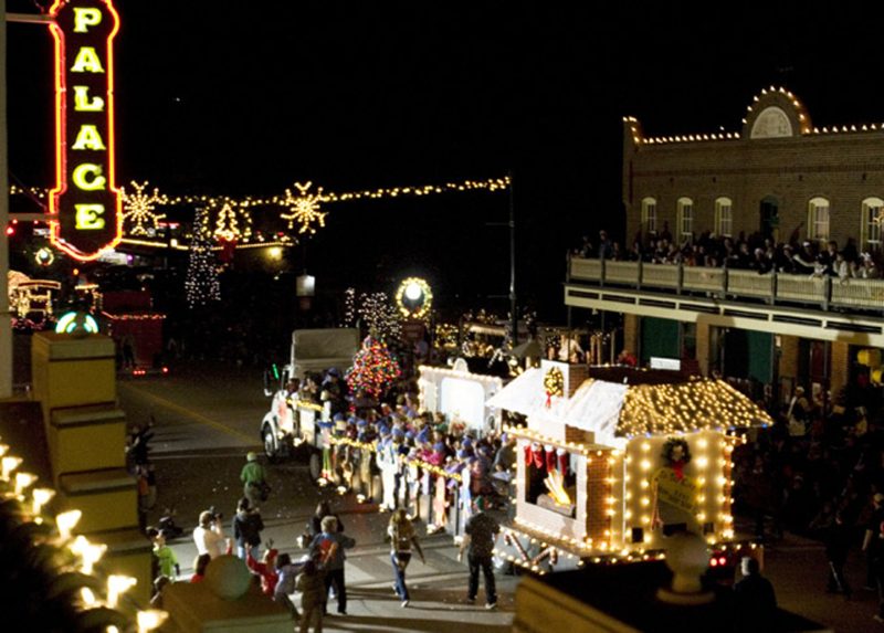 Grapevine at Christmas Parade of Lights as seen from above, a lighted float with buildings and street dressed up with holiday lights. Palace Theater sign in the upper left side of photo