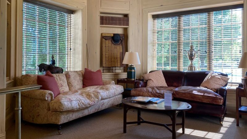 Reading nook at the National Sporting Library in Middleburg, VA is a great place to read a book with the kids. Photo shows cozy couches with throw pillows, lamps, a coffee table and windows to the grounds.