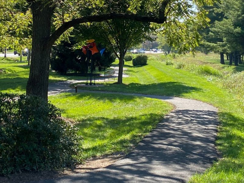 Walking path at Raflo Park in Leesburg, VA with trees, grass and art installation pictured