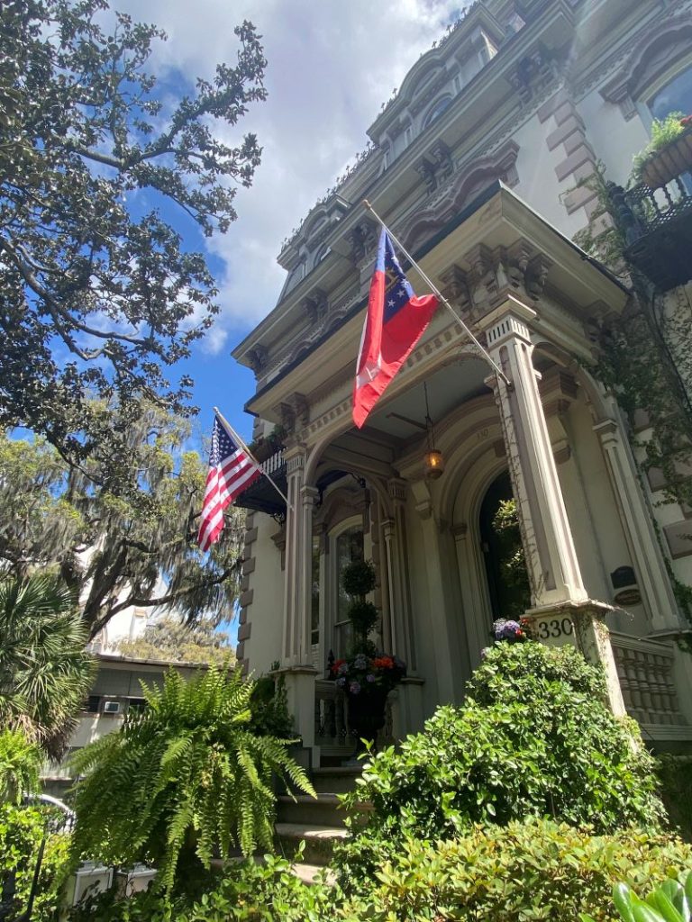 Historic building in Savannah with flags out front and lots of greenery and Spanish moss