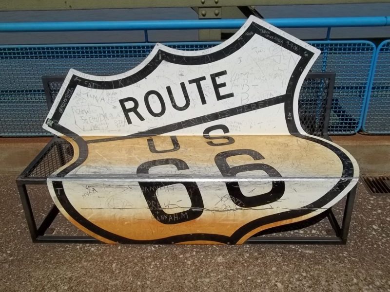 Park bench made with a historic route 66 sign. graffiti and skateboard wear and tear are visible on the black and white shield design