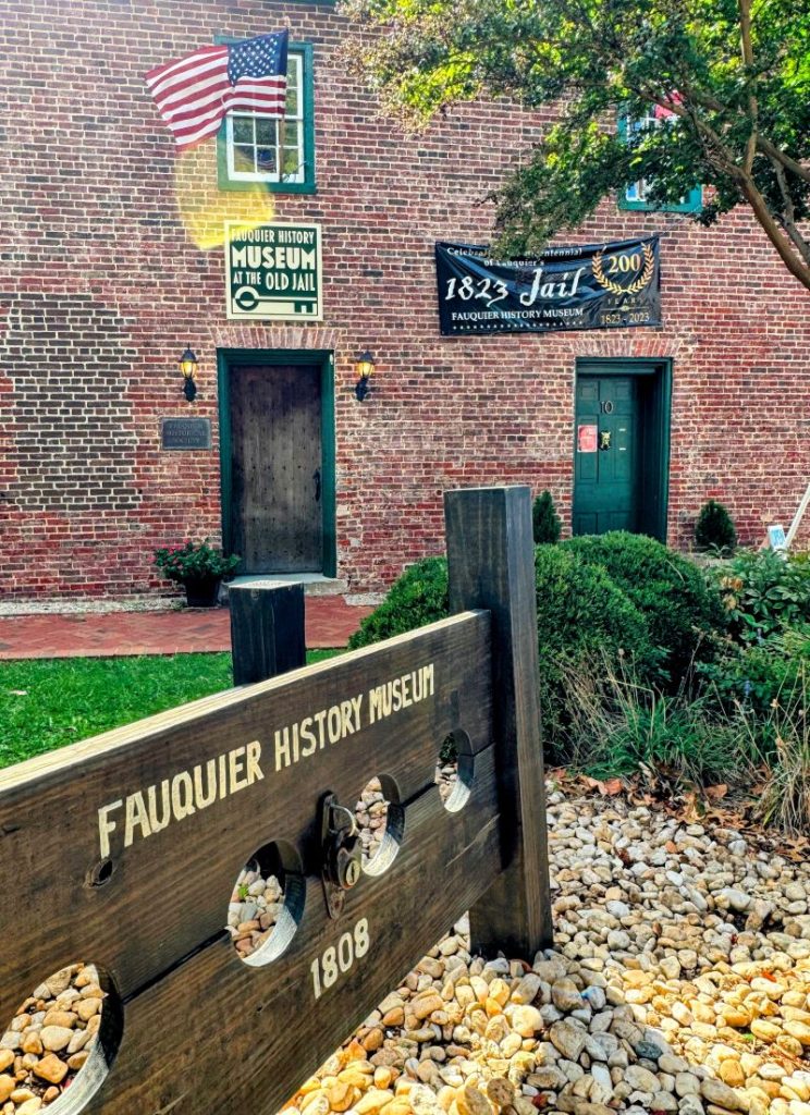 Entrance to the Fauquier History Museum at the 1808 jail in Warrenton. Brick facade with American flag and stocks out front