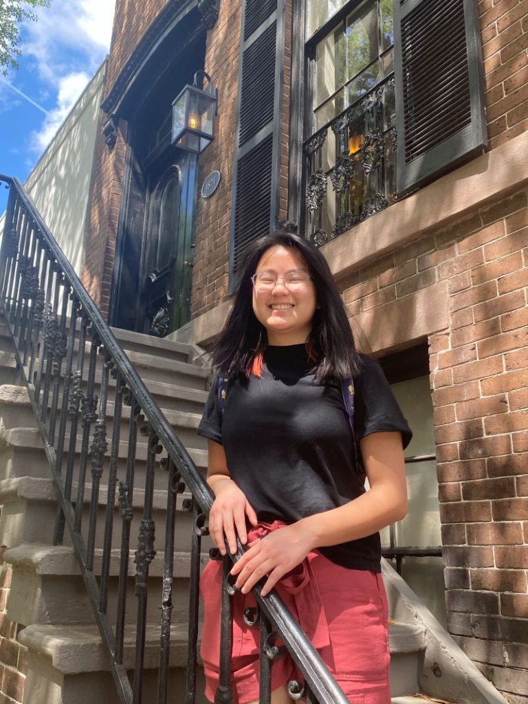 Asian girl in black t-shirt standing on a staircase in Savannah at a wrought iron railing with historic brick facade behind her