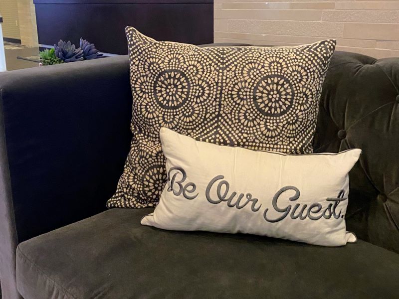 Sofa with pillows, one of which says, "Be our guest" in the lobby entrance at Archer Hotels Falls Church.