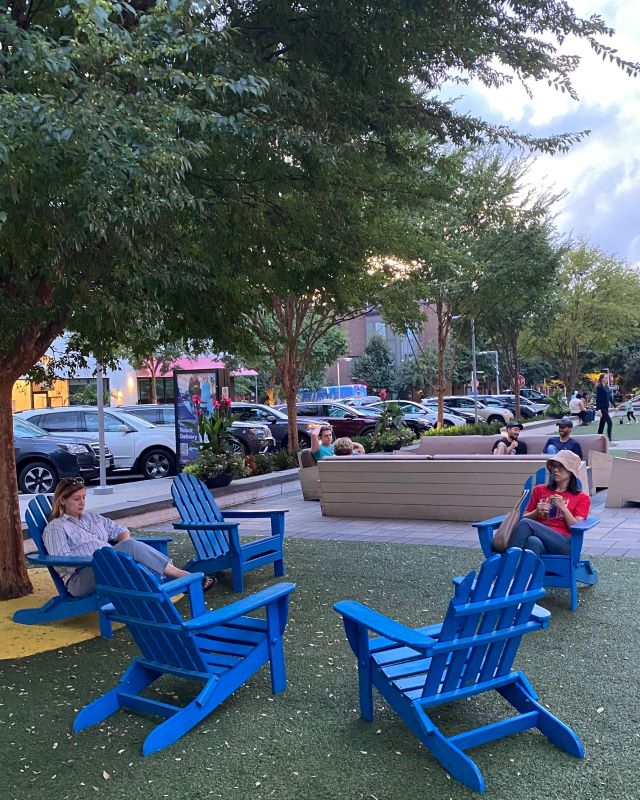 People enjoying the parklike seating areas, with two women in the front area, a group in the next seating area and kids playing on the grass behind.